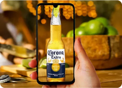 Uma m&atilde;o segurando um celular com a imagem de um garrafa de corona.